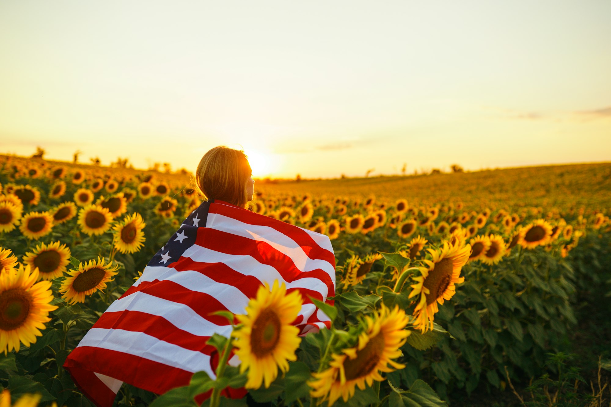 Beautiful girl with American flag in a sunflower field. 4th of July. Fourth of July. Freedom.