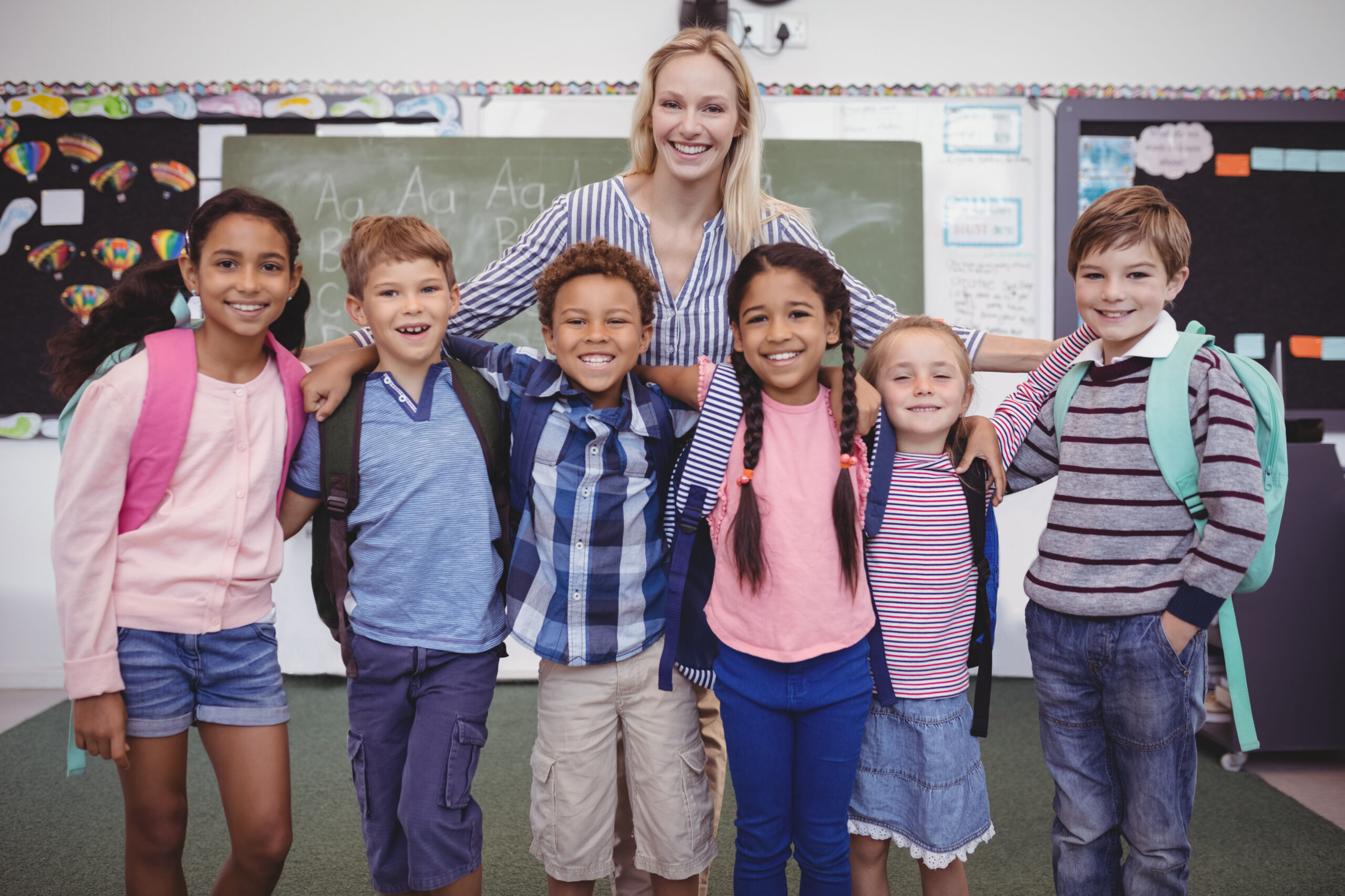 Happy teacher standing with schoolkids in classroom at school