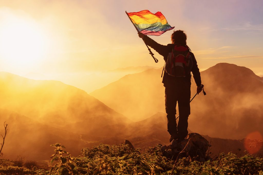 hiker with backpack and trekking poles waving an lgbt pride flag demanding the inclusion and respect of gay people in sport.