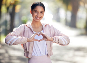 Portrait of a sporty young woman making a heart shape with her hands while exercising outdoors.