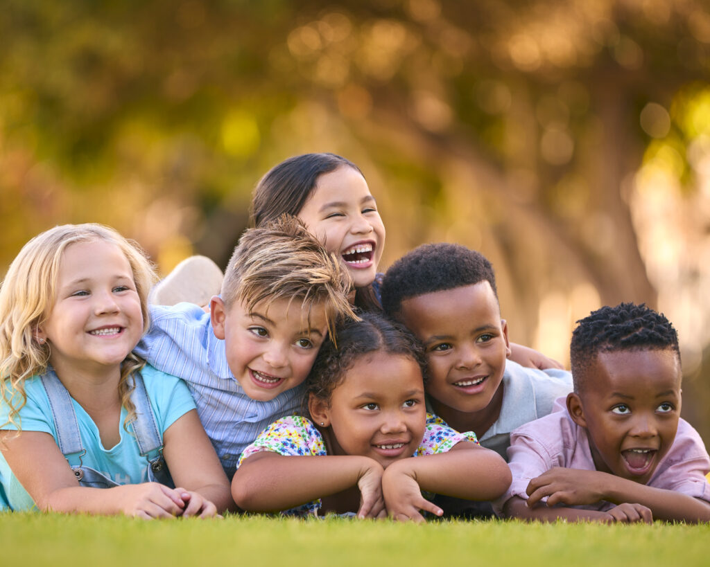 Portrait Of Multi-Cultural Primary Or Elementary School Student Friends Lying On Grass Outdoors